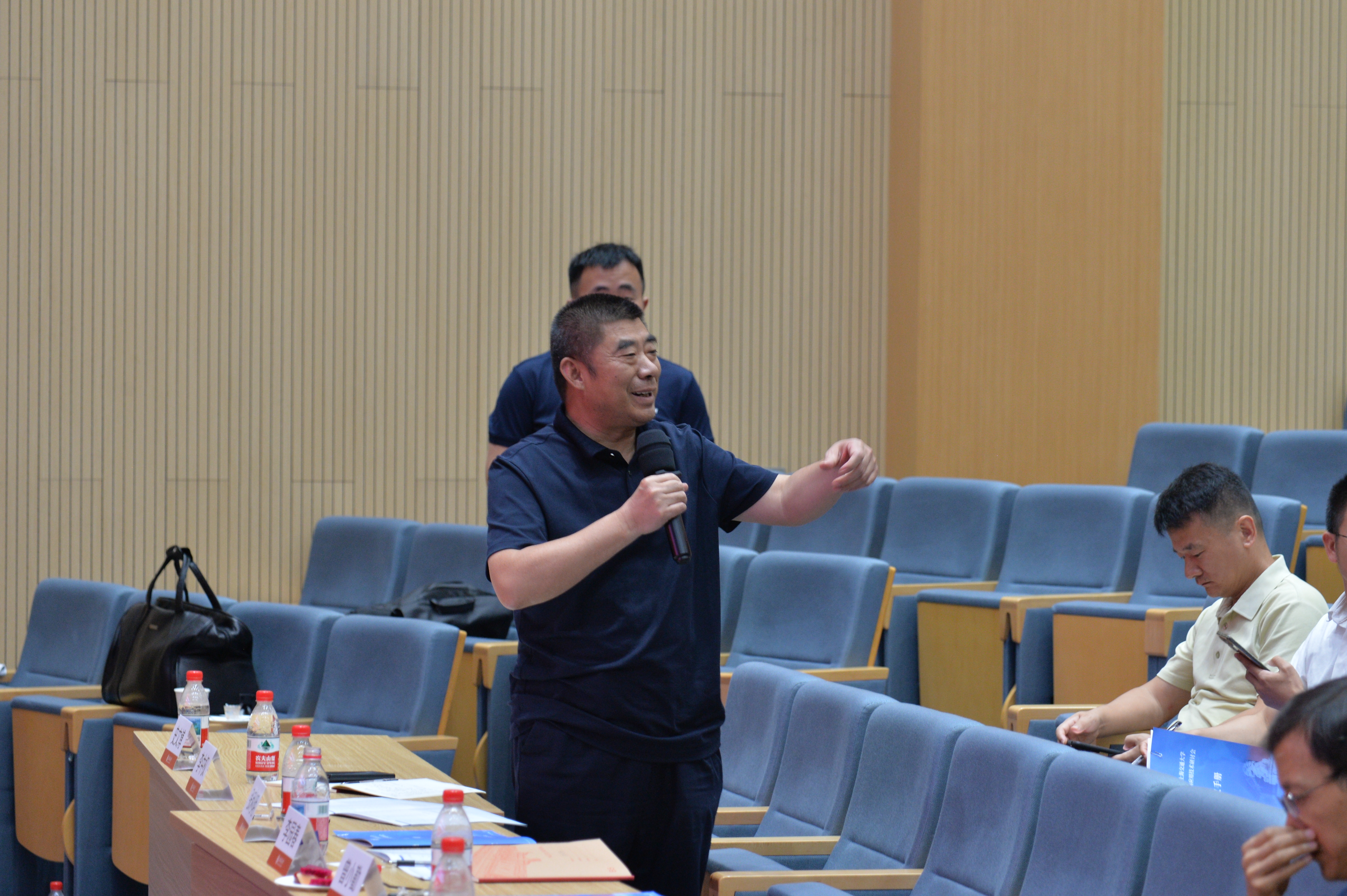 A person holding a microphone in front of a table
Description automatically generated